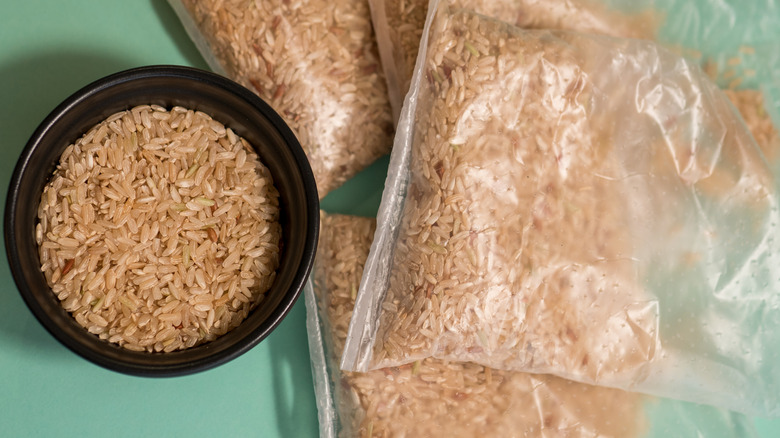 bowl of brown rice to the left of four plastic bags of uncooked brown rice