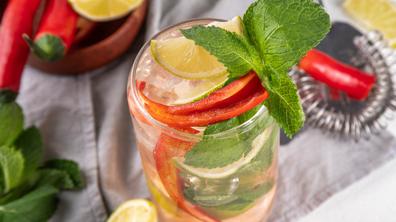 A glass of lemonade topped with peppers and fresh herbs