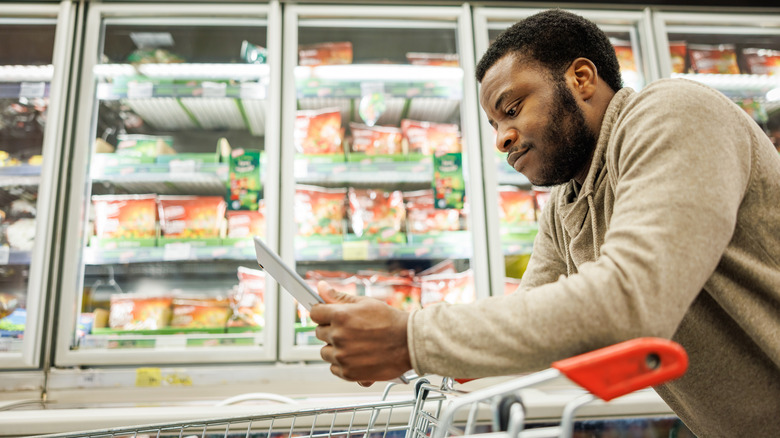 Man checking a tablet while pushing a cart in a grocery store