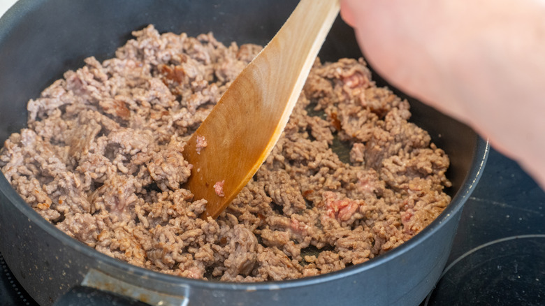 Wooden spoon stirring ground beef cooking in pan
