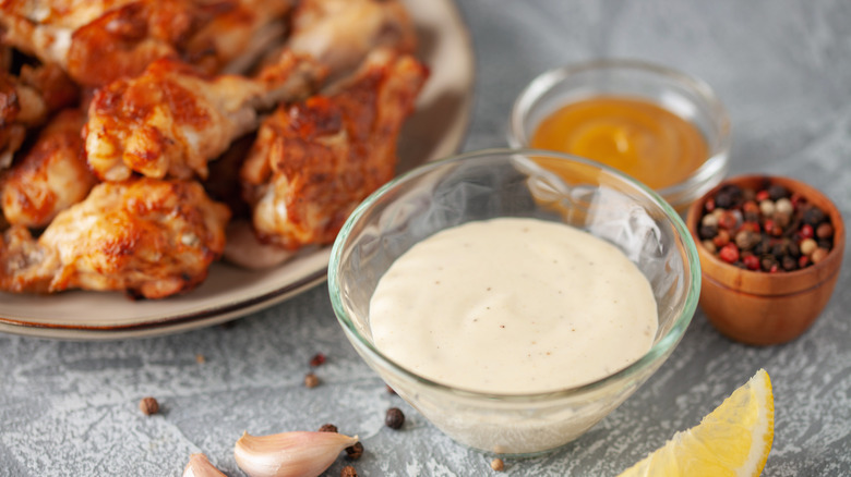 A bowl of white sauce next to chicken wings