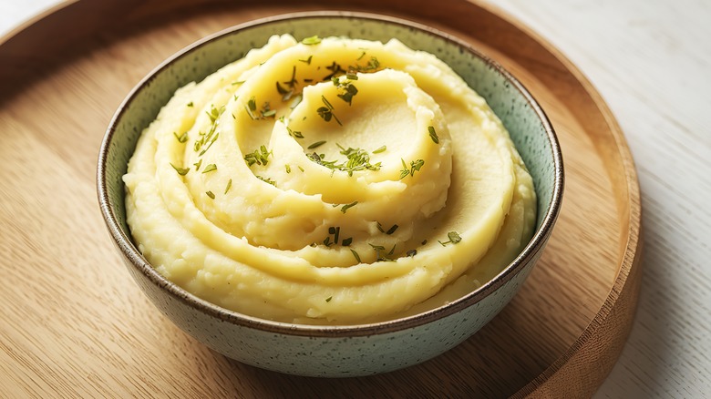 A ceramic bowl of mashed potatoes on a wood tray
