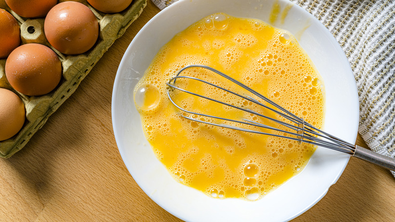 Overhead shot of a bowl of raw beaten eggs with a metal whisk lying in it