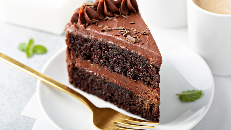 Slice of chocolate cake with gold fork on white plate