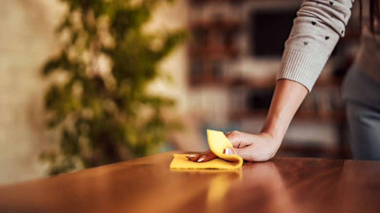 Close-up of a woman's hand wiping a dining table clean with a cloth