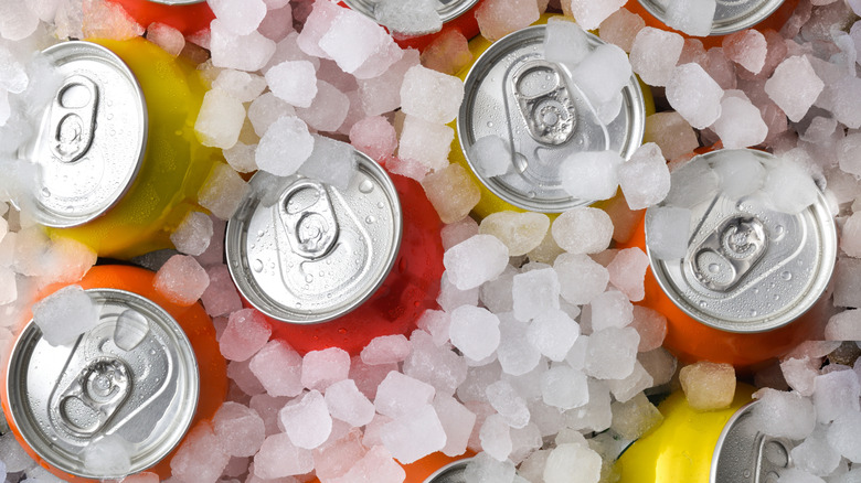 Group of cold orange, yellow, and red drink cans covered in ice. Top view.