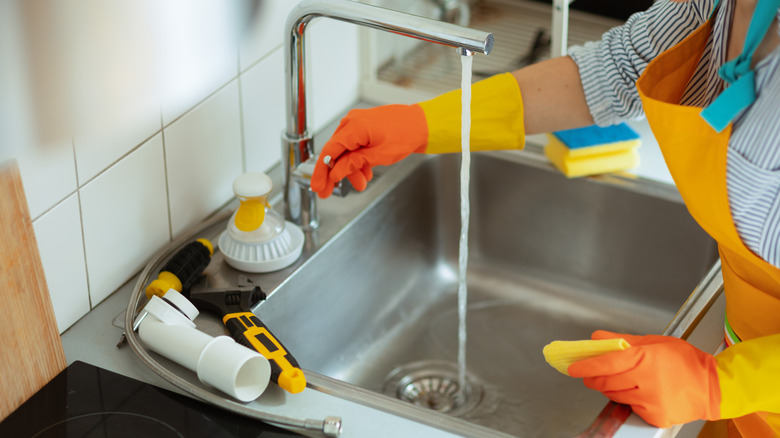 Gloved hand turns on the kitchen faucet
