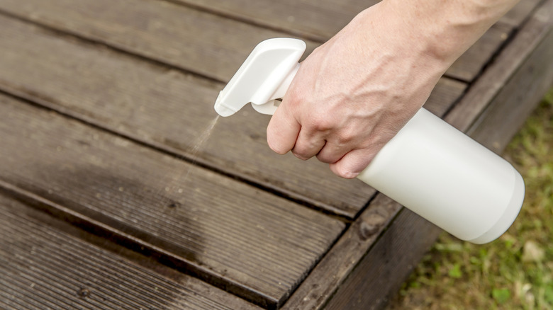 Person hand spraying insect repellent on home terrace wood boards.