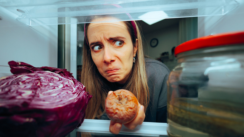 Woman with expressive concerned look Taking out a Rotten Fruit from her Fridge.