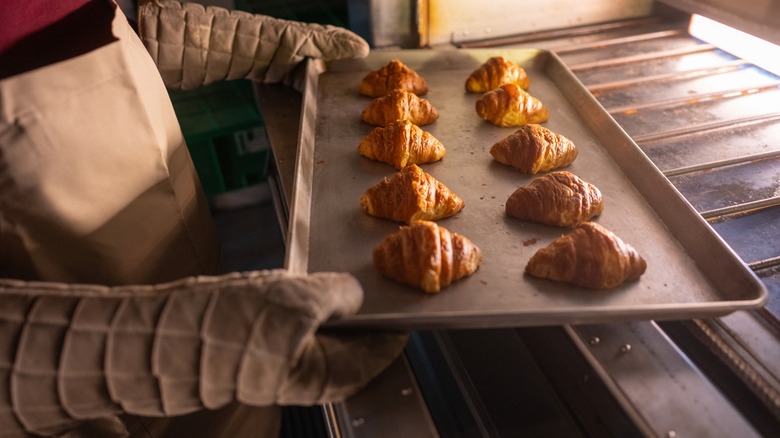 A close-up of person inserting aluminum baking sheet with croissants into oven