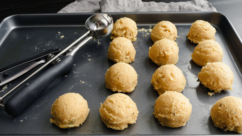 A baking sheet with a metal scoop and cookie dough balls