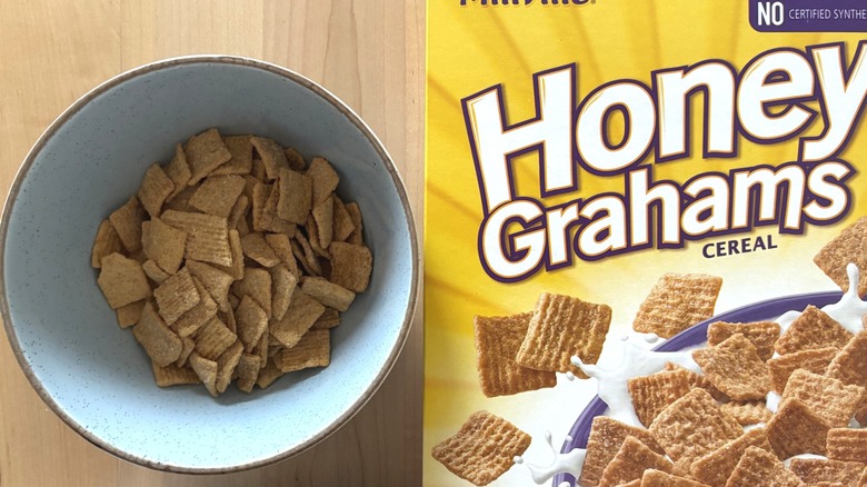 A bowl of cereal next to a box of Honey Grahams