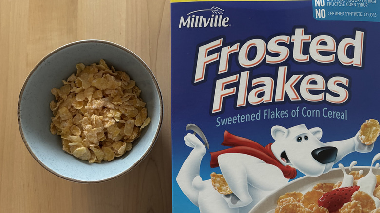 A bowl of flakes of corn cereal next to a box of Frosted Flakes