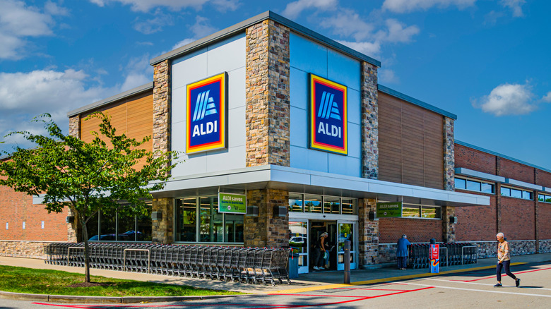 Exterior of Aldi with a customer crossing the parking lot to enter the front door
