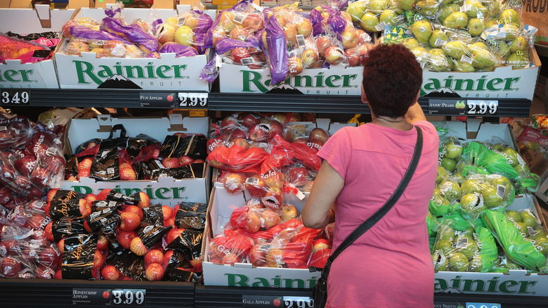 A customer shopping at an Aldi, photographed from behind in front of a display of apples