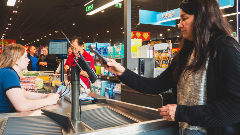 A woman pays at an Aldi checkout counter while the cashier sits and other shoppers stand in line.