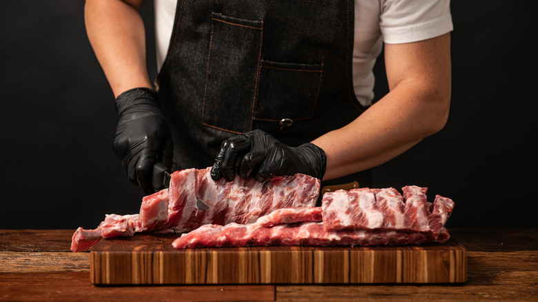 A butcher separates a rack of pork ribs on a wood cutting board.