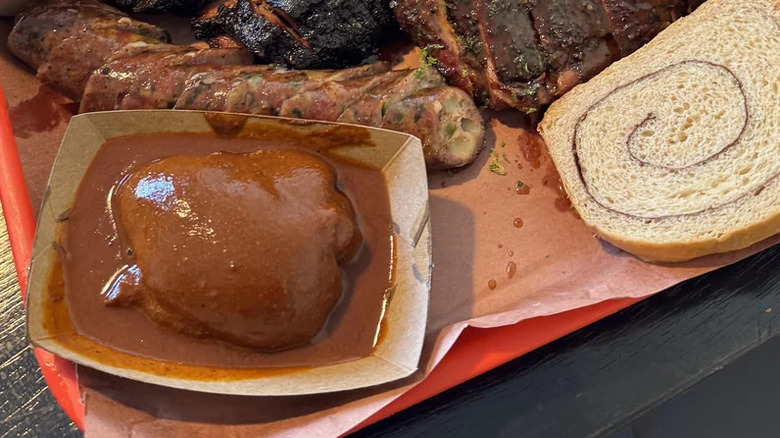 chicken thigh in mole sauce at barb's b q on a red tray next to sides of bread and other smoked meats