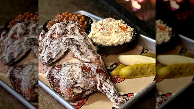 Tray of Big Bob Gibson's famous smoked chicken in Alabama white sauce with side of baked beans, potato salad, and pickles.