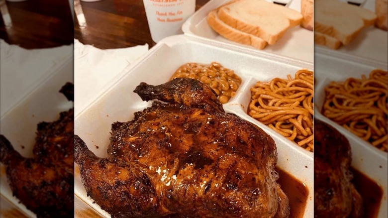 cozy corner's whole barbecued cornish hen in a pool of juice in a styrofoam takeout box next to a side of spaghetti, bread, and beans