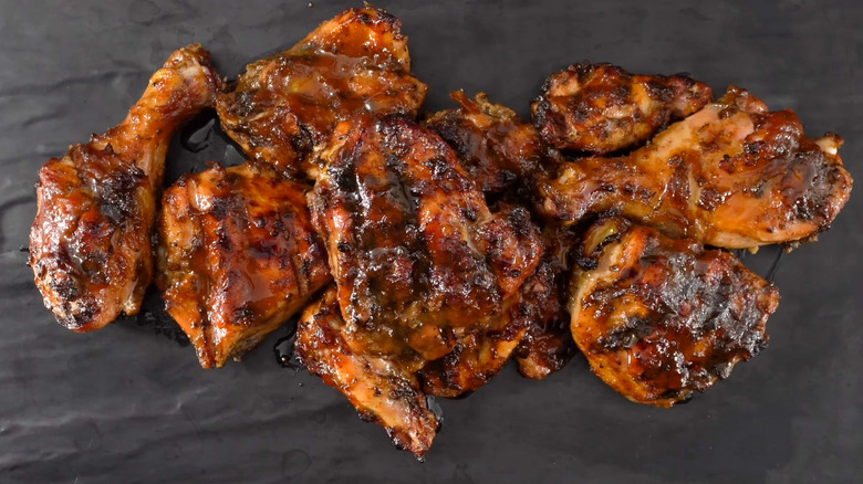 a pile of saucy barbecue chicken drumsticks, thighs, and wings on a stone plate