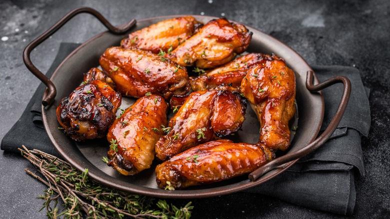 plate of bbq chicken wings on a black napkin, next to a few sprigs of thyme
