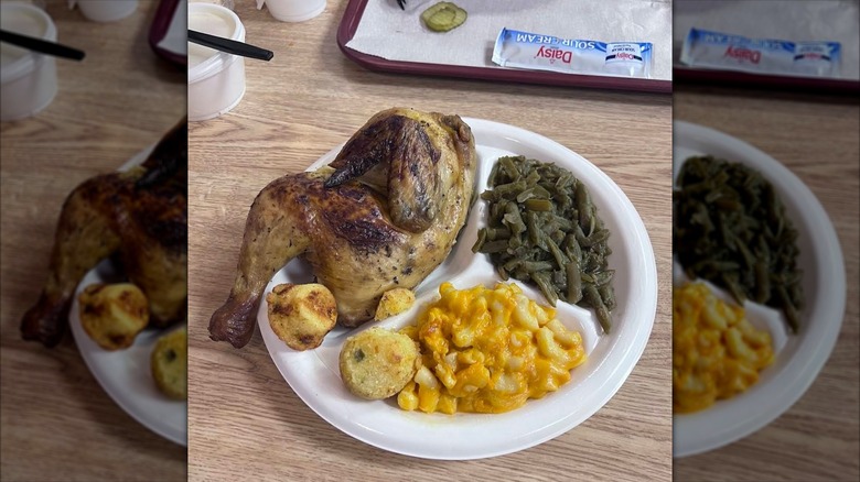 styrofoam plate of roasted half chicken from rustys bar b q next to cornbread muffins, mac and cheese, and green beans