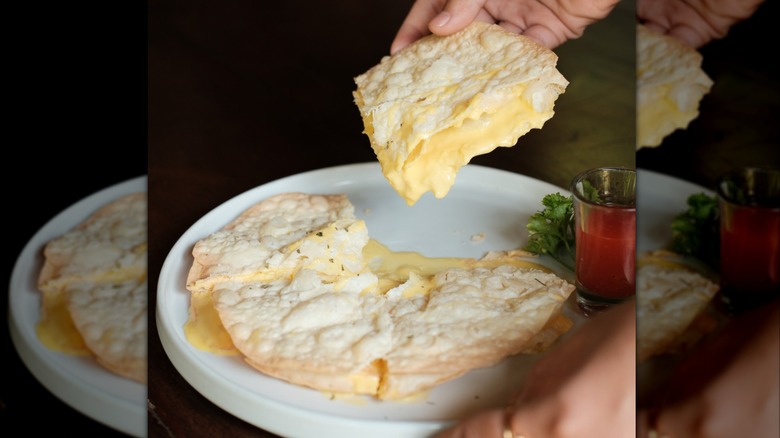 Delicious cheesy quesadilla with dripping cheese, held over a white ceramic plate with a drink on the side