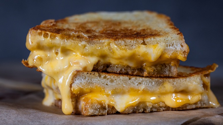 Grilled Cheese with melting cheese dripping from the inside. The sandwich is cut in half and placed on a wooden cutting board