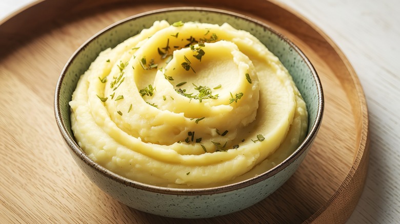 A photo of seasoned mashed potatoes in a bowl, resting on a wooden plate