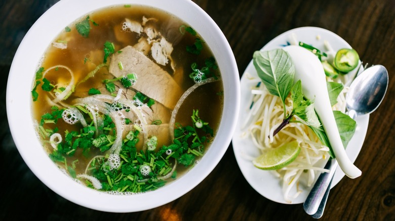 Pho noodle soup in broth with rice noodles, beef, and fresh vegetables like cilantro, Thai basil, and bean sprouts.