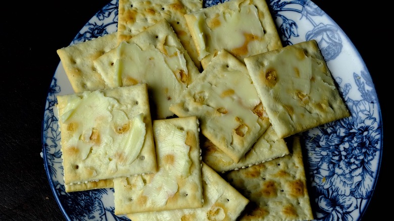 Top-down view of buttered saltine crackers on a blue plate