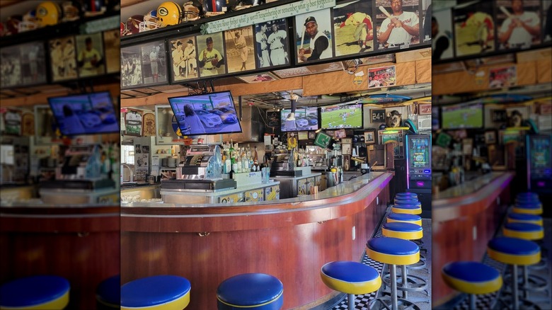 An empty old-school dive bar with a horsehoe-shaped bar and blue and yellow backless barstools