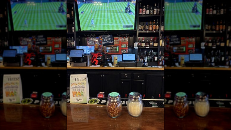 A view of the back bar at Pizzaville, a red peper flake shaker and Parmesan shaker in the forefront