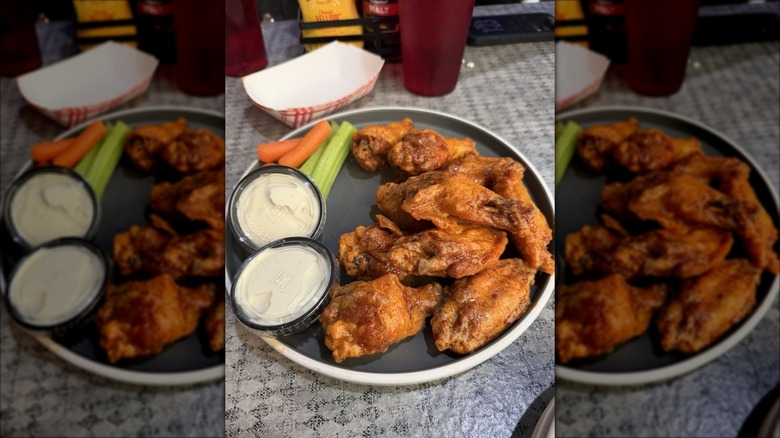 A plate of chicken wings on a gray plate with two plastic ramekins of dressing
