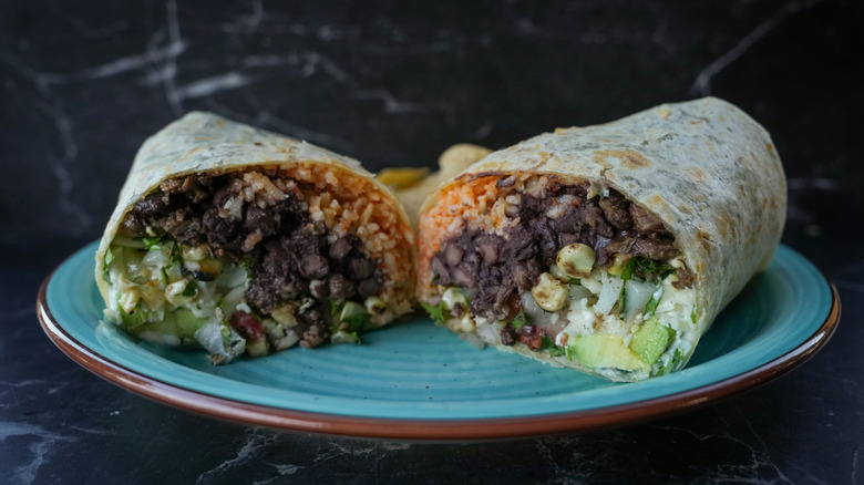 Burrito with black beans, rice, and vegetables with a dark background.