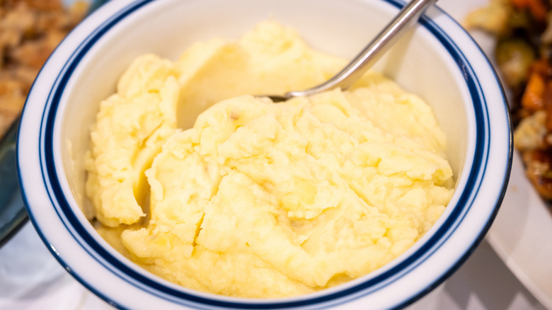 A white bowl with a blue trim filled with creamy mashed potatoes.