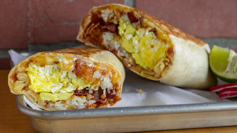Eggs, bacon, and cheese wrapped in a toasted tortilla on a silver tray.
