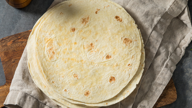A stack of homemade flour tortillas on a kitchen towel.