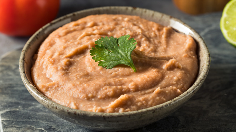An earthen bowl with refried pinto beans garnished with a cilantro leaf.