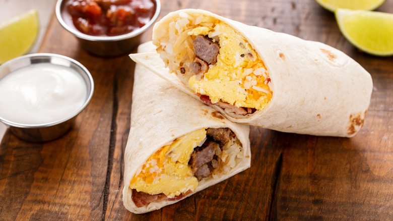 Simple breakfast burrito with eggs, sausage, and cheese on a wooden platter.