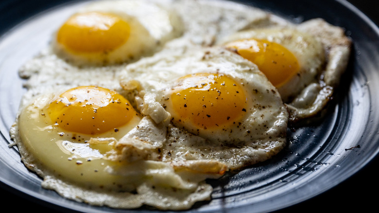 Four fried eggs with runny orange yolks on a dark plate.