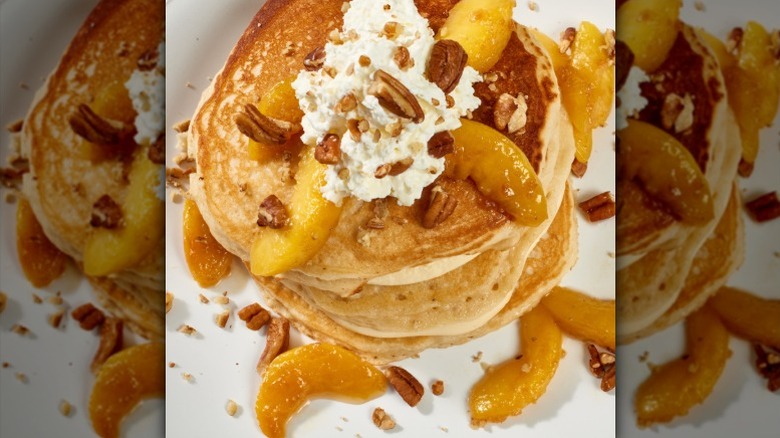 A stack of pancakes with peaches, pecans, and whipped cream on white plate from Another Broken Egg Cafe