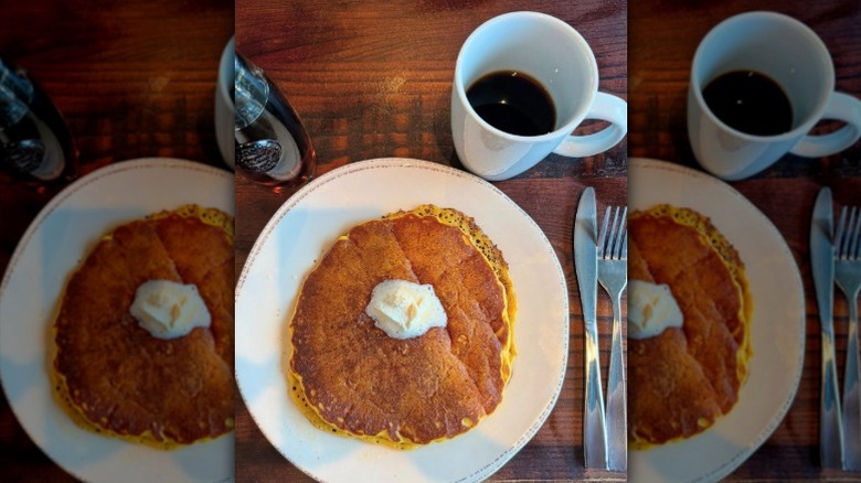 A stack of pancakes from First Watch on wooden table with white mug of coffee