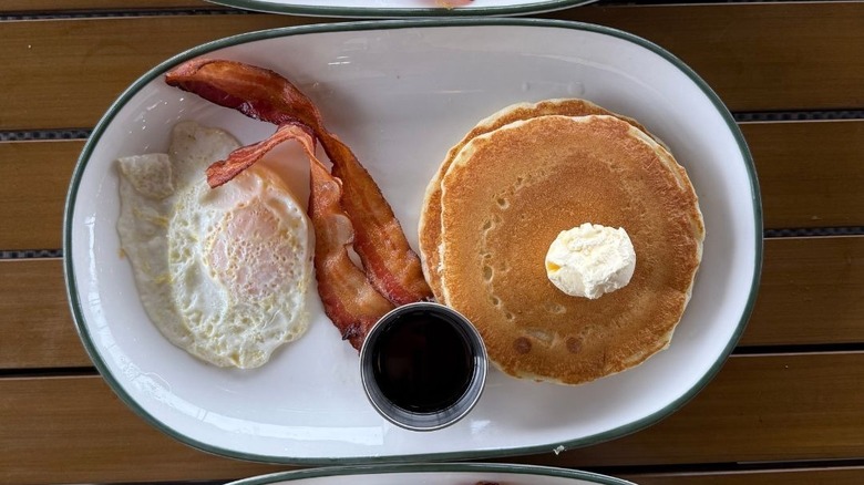Two pancakes on white plate with side of syrup, bacon, and egg at Perkins