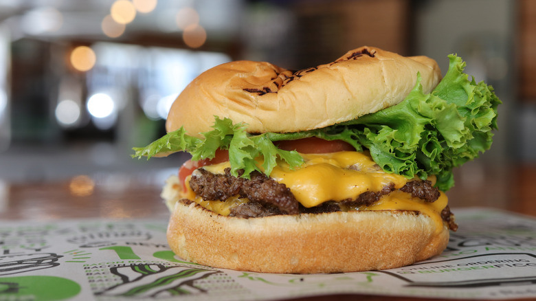 burger from burgerfi with lettuce, cheese, and tomato, placed on paper with an out of focus background