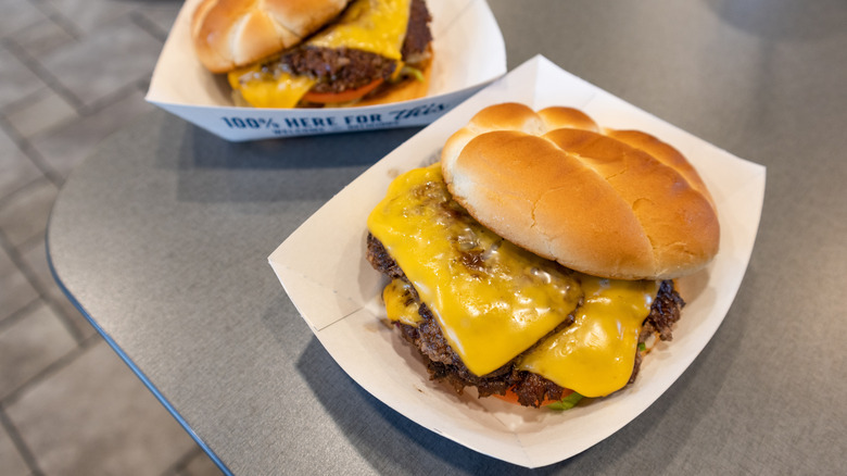Two culver's cheeseburgers on paper plates sitting on a gray table