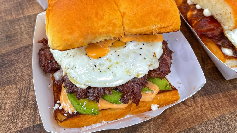 smashburger from Dog Haus with fried eggs, sauce, and avocado on a paper plate