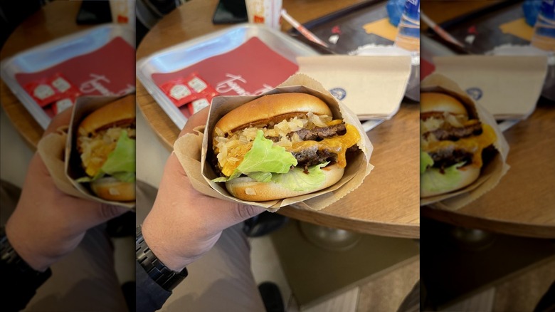 Hand holding an elevation burger with lots of toppings and cheese