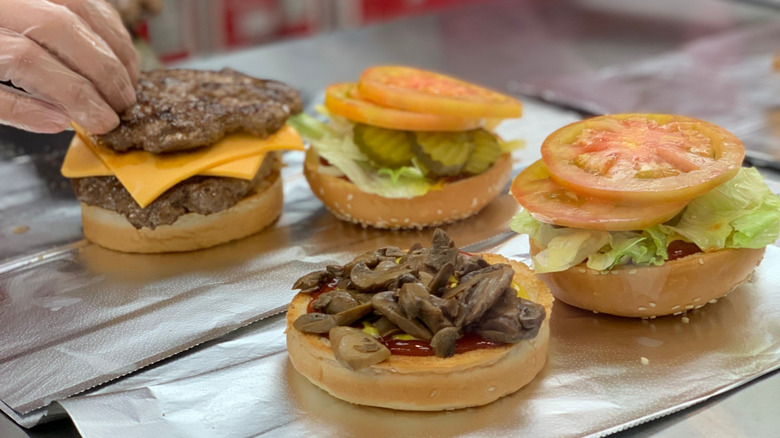 employee at five guys wearing a plastic glove preparing two burgers with tons of toppings